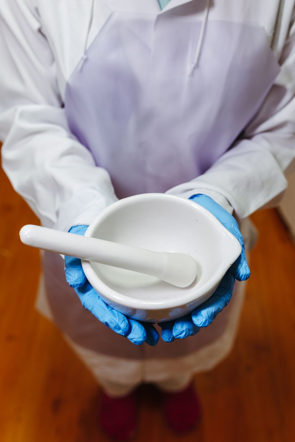 A compounding pharmacist in gloves and a lab coat holding a mortar and pestle