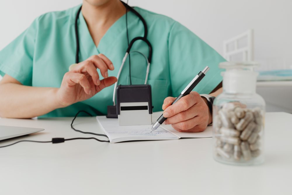 A clinician in scrubs writing a prescription at a desk
